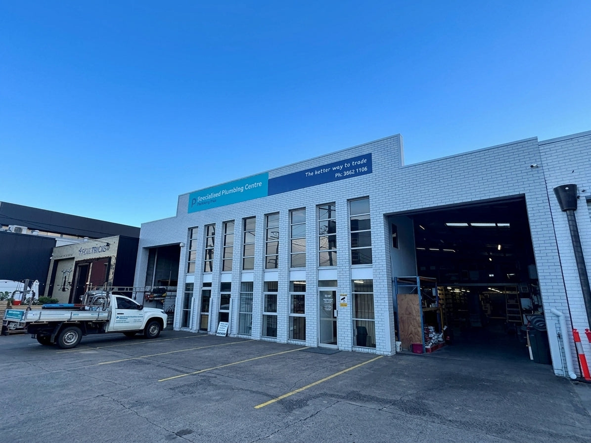 A white brick commercial building with large garage-style doors, glass windows, and a blue sign reading 'Specialist Flooring Centre' under a blue sky.